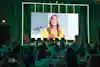 a group of people sitting at tables and a large screen with a woman on it