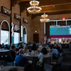 a group of people sitting at tables in a room with a stage and chandeliers