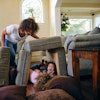 a woman pushing a child under a couch