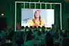 a group of people sitting at tables and a large screen with a woman on it