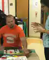 a man sitting at a table with a man in orange shirt
