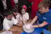 a group of kids and a woman holding a bowl of liquid