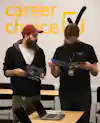 two men standing in a room reading a book