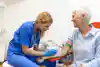 Preparation for blood test with senior woman by female doctor medical uniform on the table in white bright room. Nurse pierces the patient's arm vein with needle blank tube.