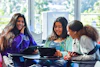 a group of girls sitting at a table looking at a tablet